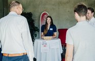 Vier Menschen stehen lachend um einen Ausstellungstisch, auf welchem ein Produkt präsentiert wird