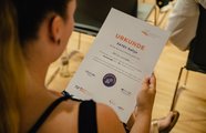 Eine Frau steht mit dem Rücken zur Kamera und hält eine Urkunde in der Hand, die sie anschaut
