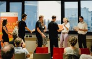 Ein Publikum schaut auf Menschen auf der Bühne, denen gerade ein Zertifikat überreicht wird