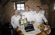 Drei Jugendliche und ein kleiner Hund lächeln in die Kamera und präsentieren ihr Produkt