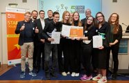 Viele Menschen stehen auf der Bühne, einige halten Zertifikate in die Kamera und lächeln