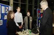 Drei Jugendliche hinter ihrem Ausstellungstisch, die sich mit einem Mann unterhalten