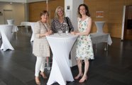 Drei Frauen stehen lächelnd um einen Stehtisch