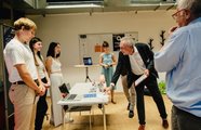 Ein Team steht hinter einem Ausstellungstisch, auf welchem ihre Start-up Idee liegt, zwei Männer begutachten das Produkt