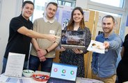 Ein Team, bestehend aus vier Personen, präsentiert lächelnd sein Produkt