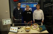 Drei Jungs stehen hinter einem Ausstellungstisch, auf dem Sportequipment liegt