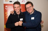 Ein Mann hat den Arm um die Schulter eines Studierenden gelegt und beide posieren ihre Fäuste aneinander geballt und lächelnd für die Kamera