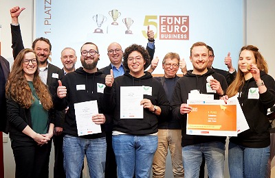 Gruppenbild: Business Mentors und Siegerteam jubeln auf der Bühne. Die Studierenden halten Zertifikate und einen Scheck über das Preisgeld in der Hand.