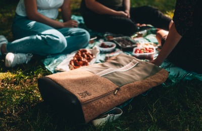 Ein Rucksack der neben einer Gruppe von Menschen am Boden liegt, die ein Picknick machen